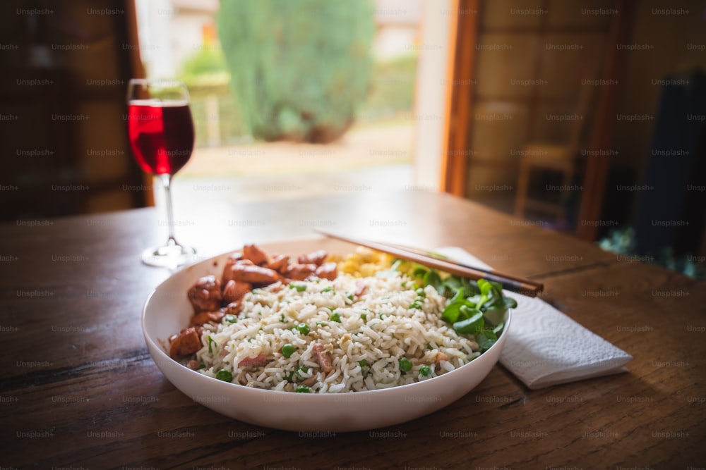 a bowl of rice, meat, and vegetables with a glass of wine