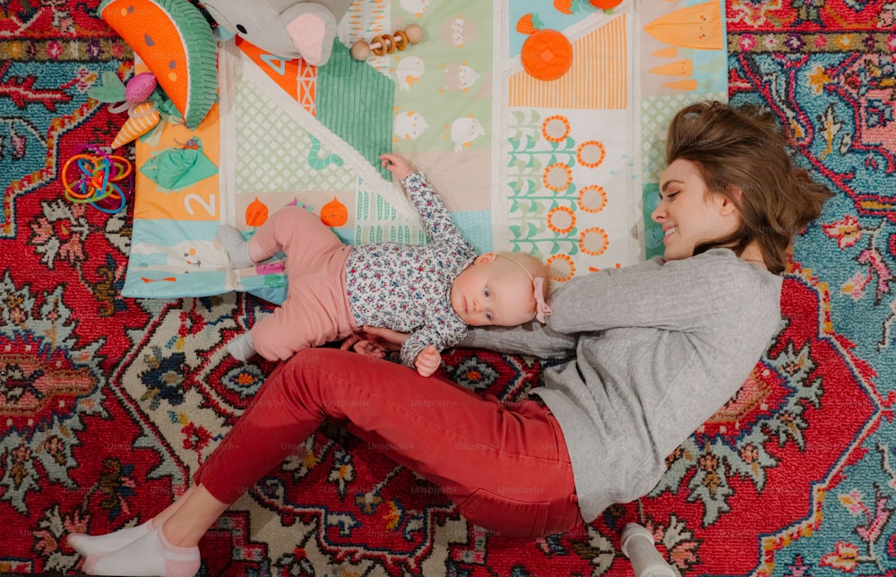 a woman laying on a rug holding a baby