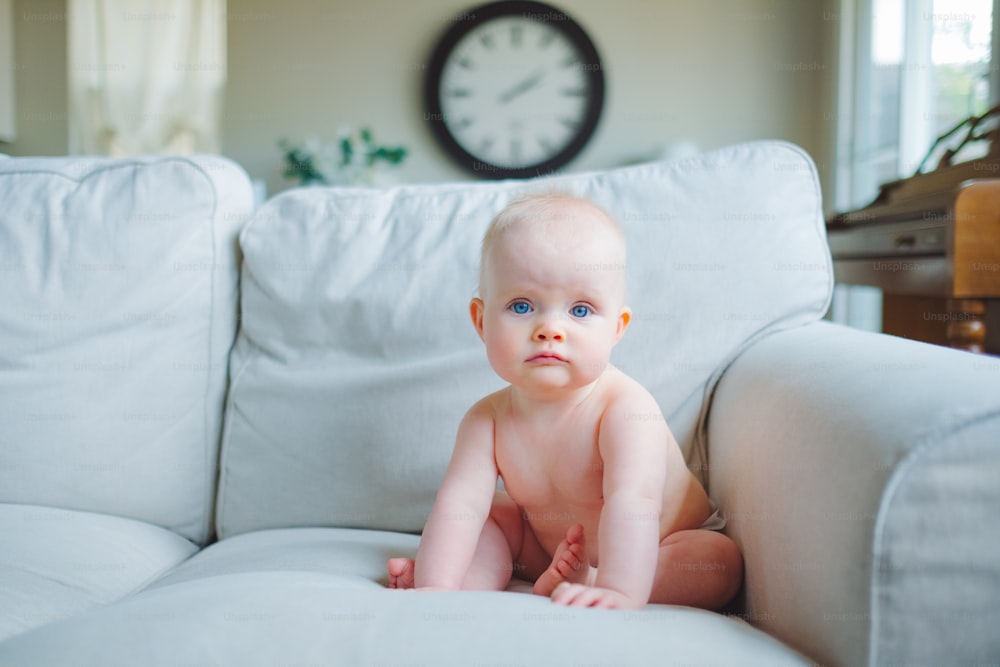 a baby sitting on a couch with a clock in the background