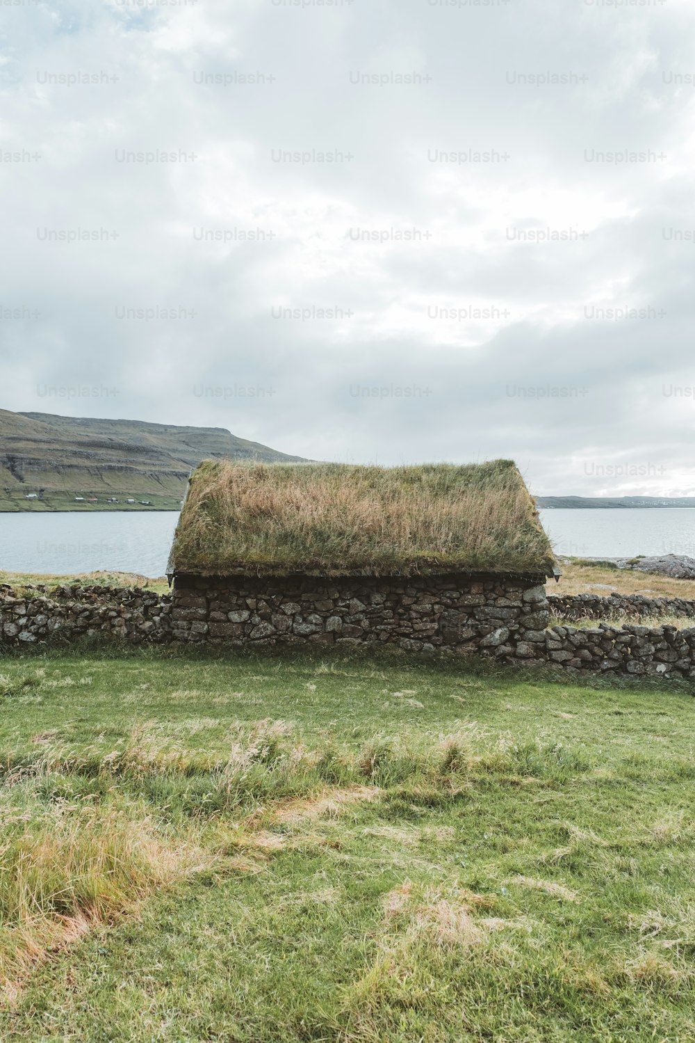 a stone wall with a grass roof next to a body of water
