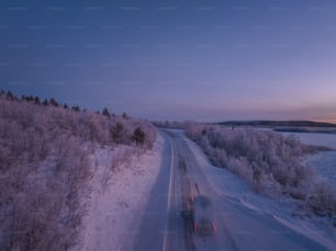 um caminhão dirigindo por uma estrada nevada ao lado de uma floresta