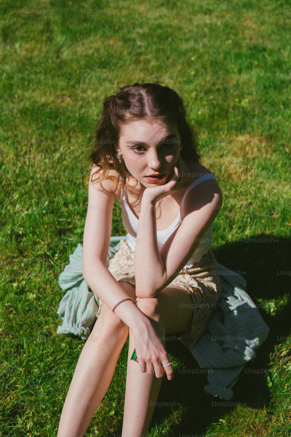 uma jovem sentada na grama com a mão no queixo