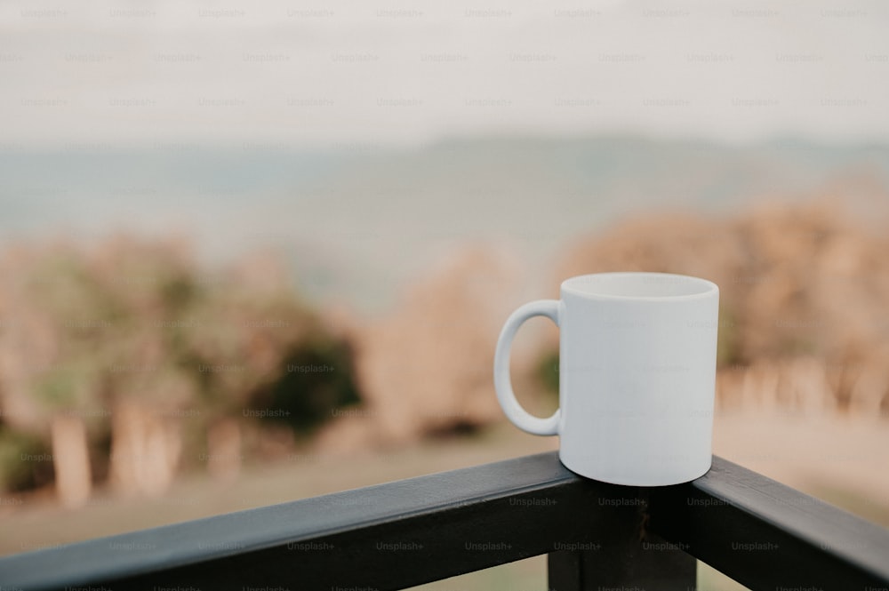 a white coffee cup sitting on top of a wooden rail