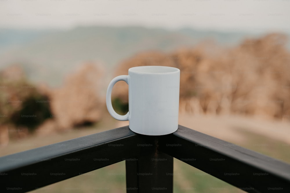 a white coffee cup sitting on top of a wooden rail