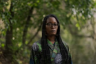 a woman wearing glasses standing in a forest