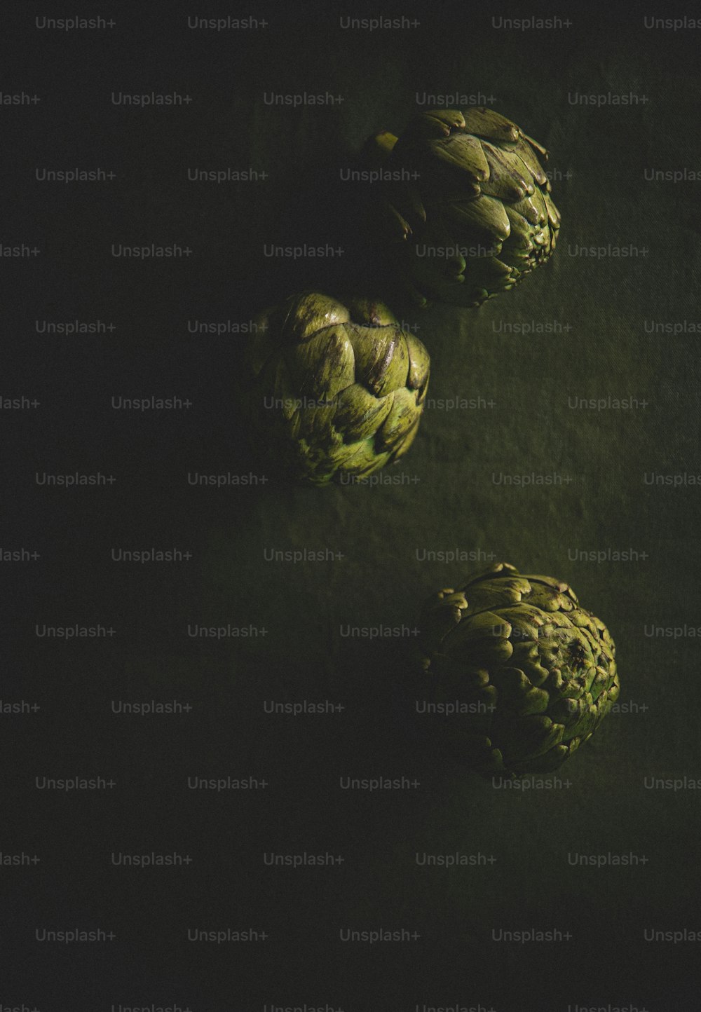 three artichokes on a dark surface with a black background