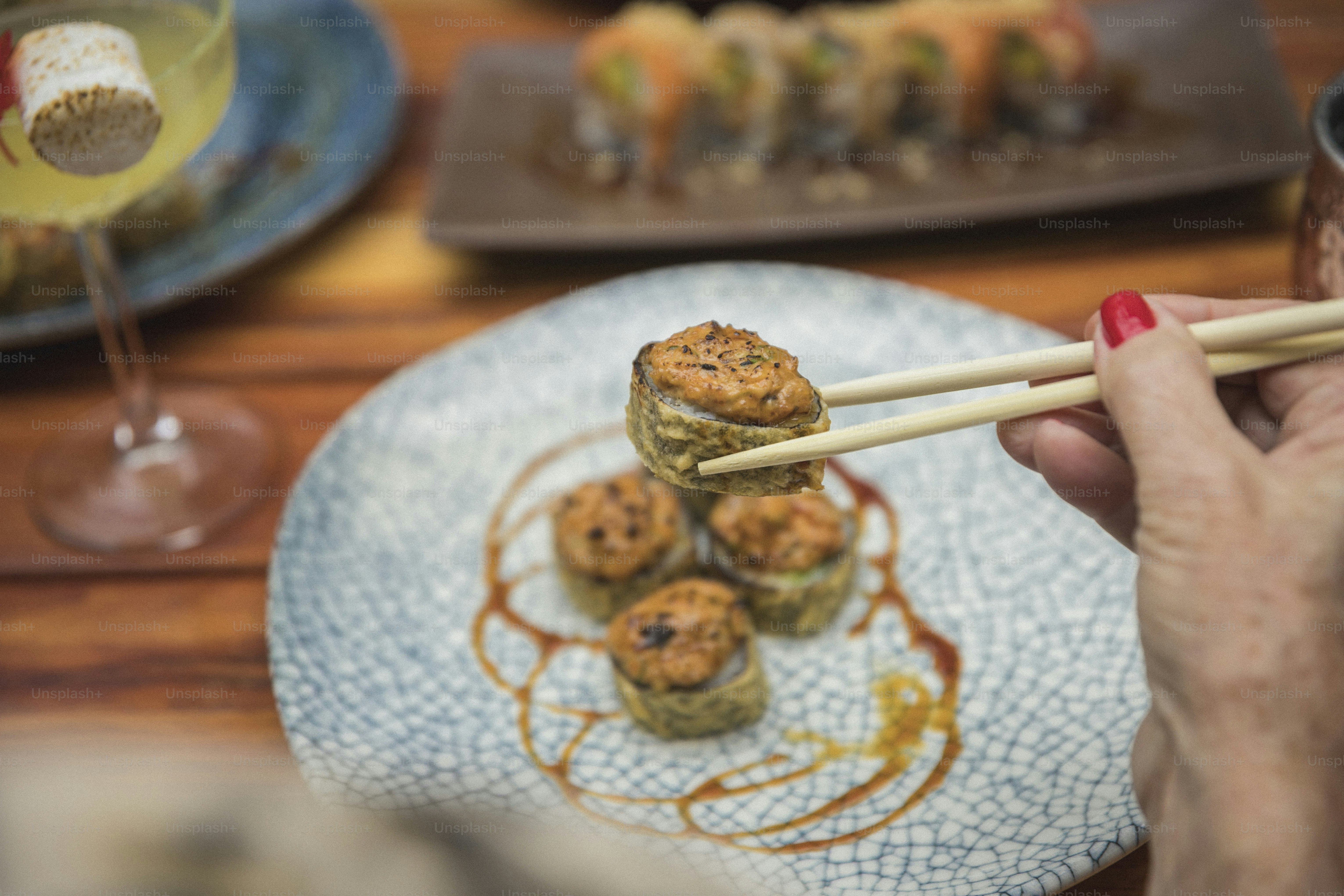 eine Person, die Essstäbchen über einen Teller mit Essen hält
