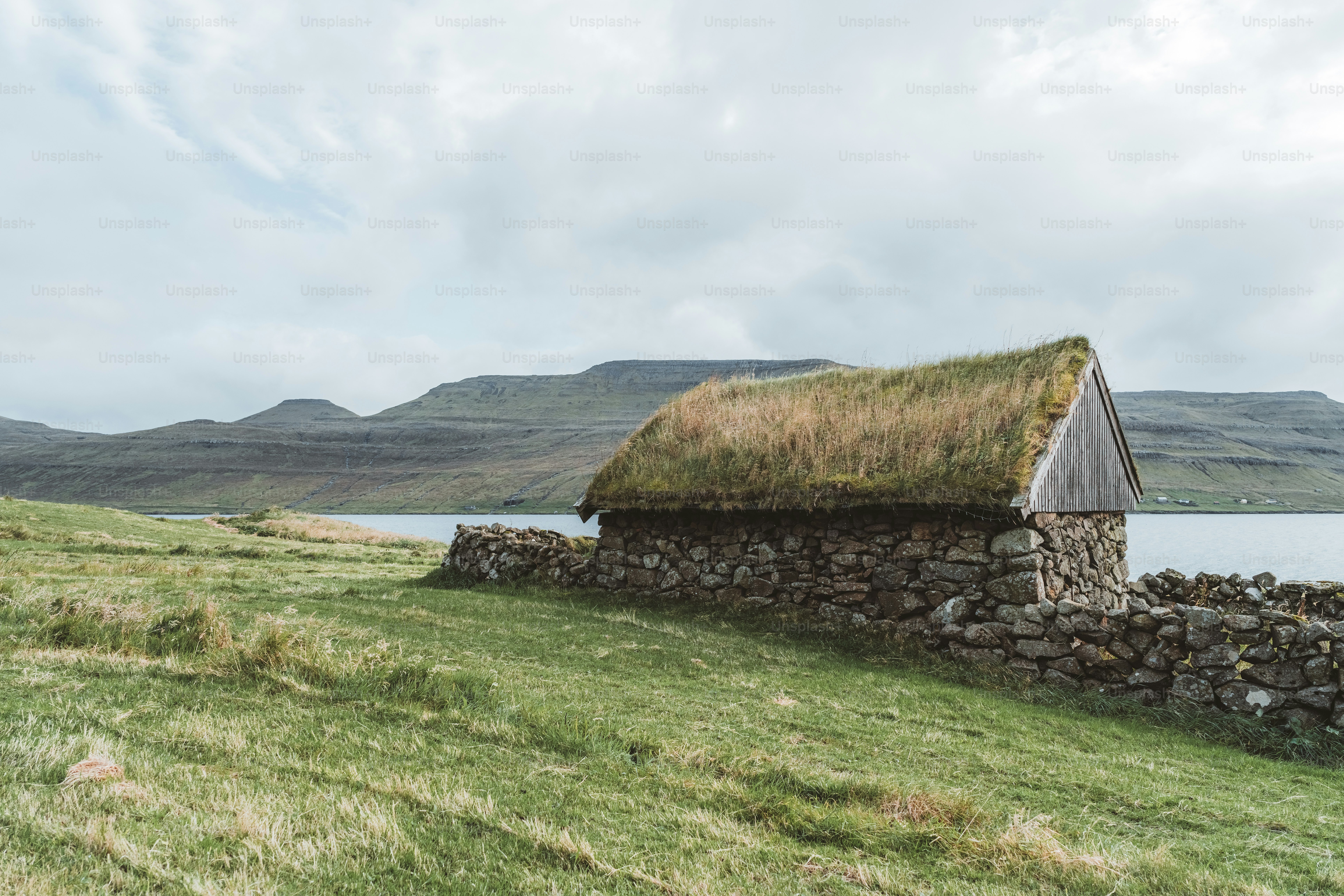 un muro de piedra con un techo de hierba junto a un cuerpo de agua