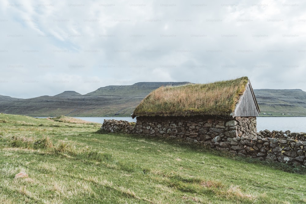 a stone wall with a grass roof next to a body of water