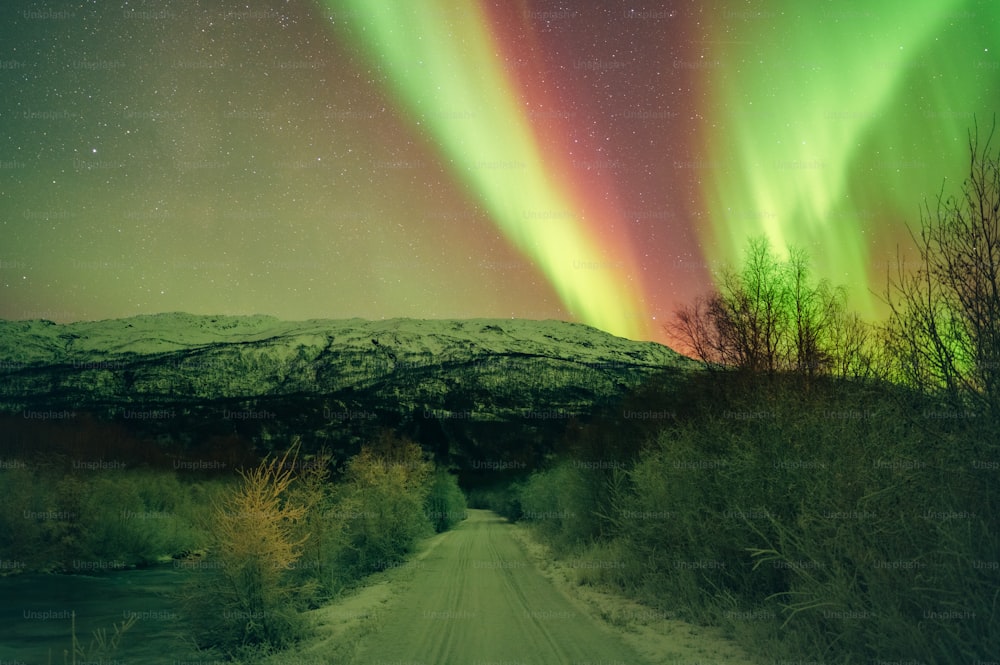 uma aurora verde e vermelha sobre uma estrada de terra