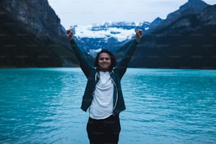 a woman standing in front of a lake with mountains in the background