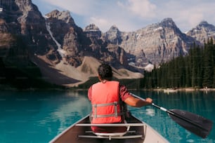 a person paddling a canoe on a lake with mountains in the background