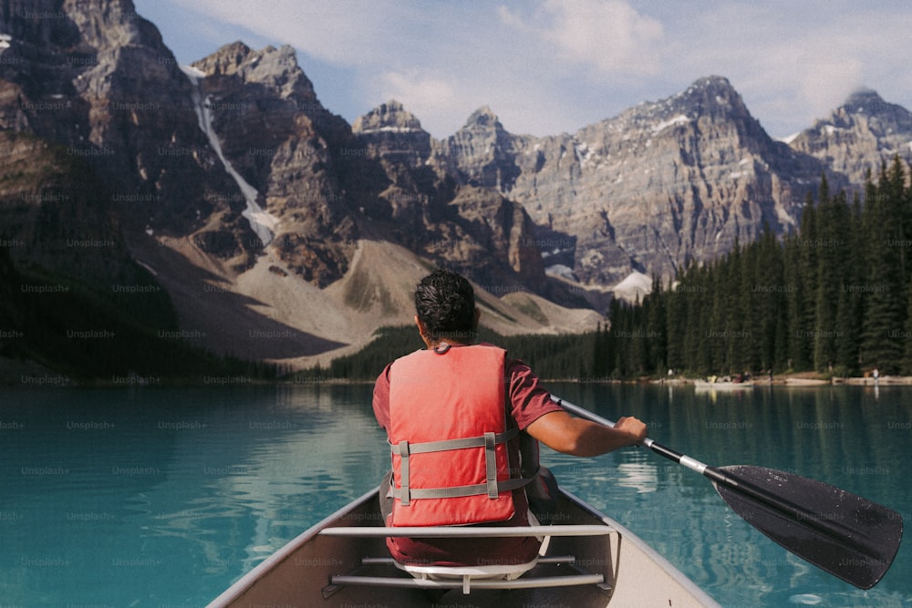 a person paddling a canoe on a lake with mountains in the background