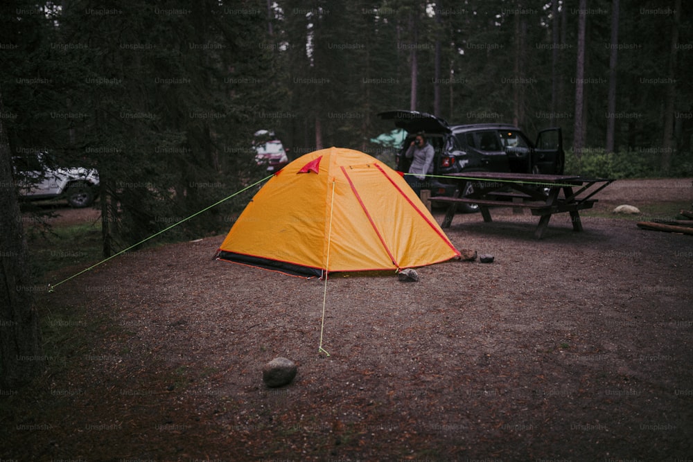 uma tenda montada na floresta ao lado de uma mesa de piquenique