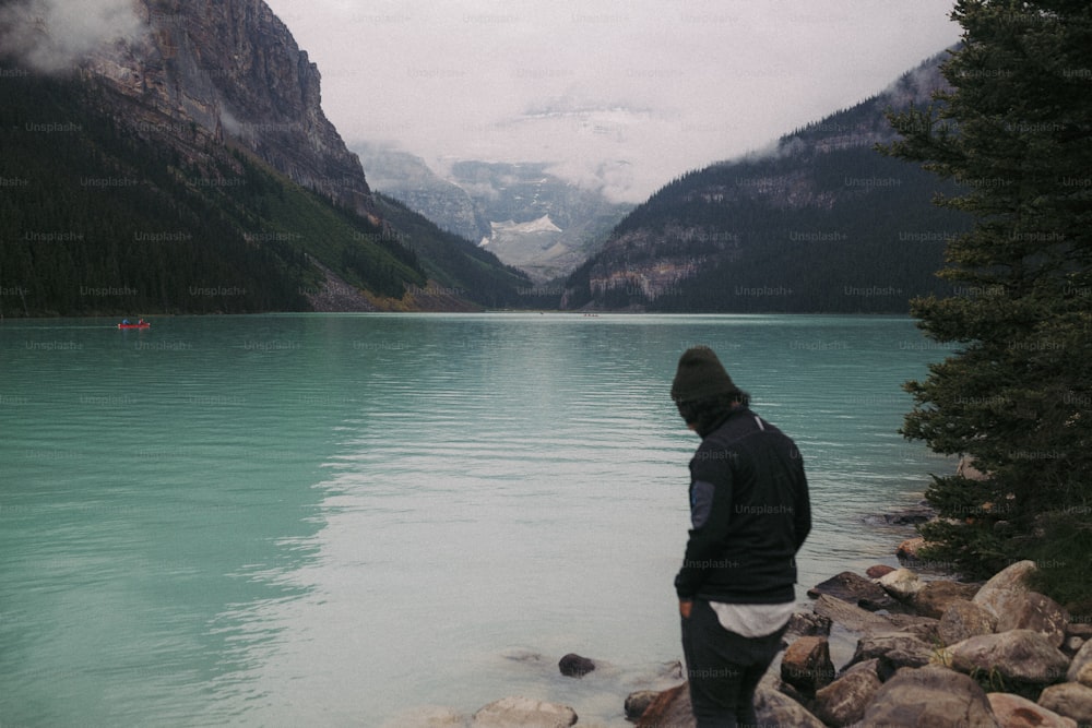 a man standing on a rocky shore next to a body of water