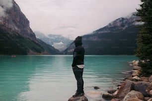 uma pessoa em pé em uma rocha perto de um corpo de água