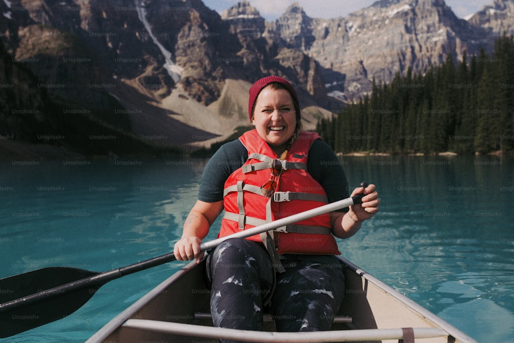 a woman in a red life jacket paddling a canoe