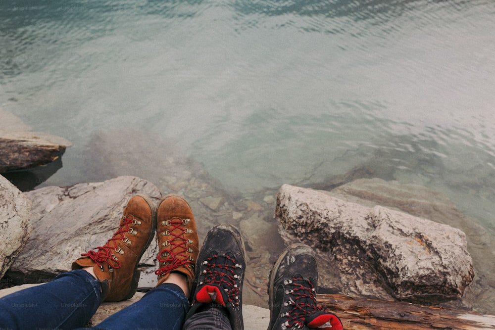 a pair of feet sitting on a rock next to a body of water