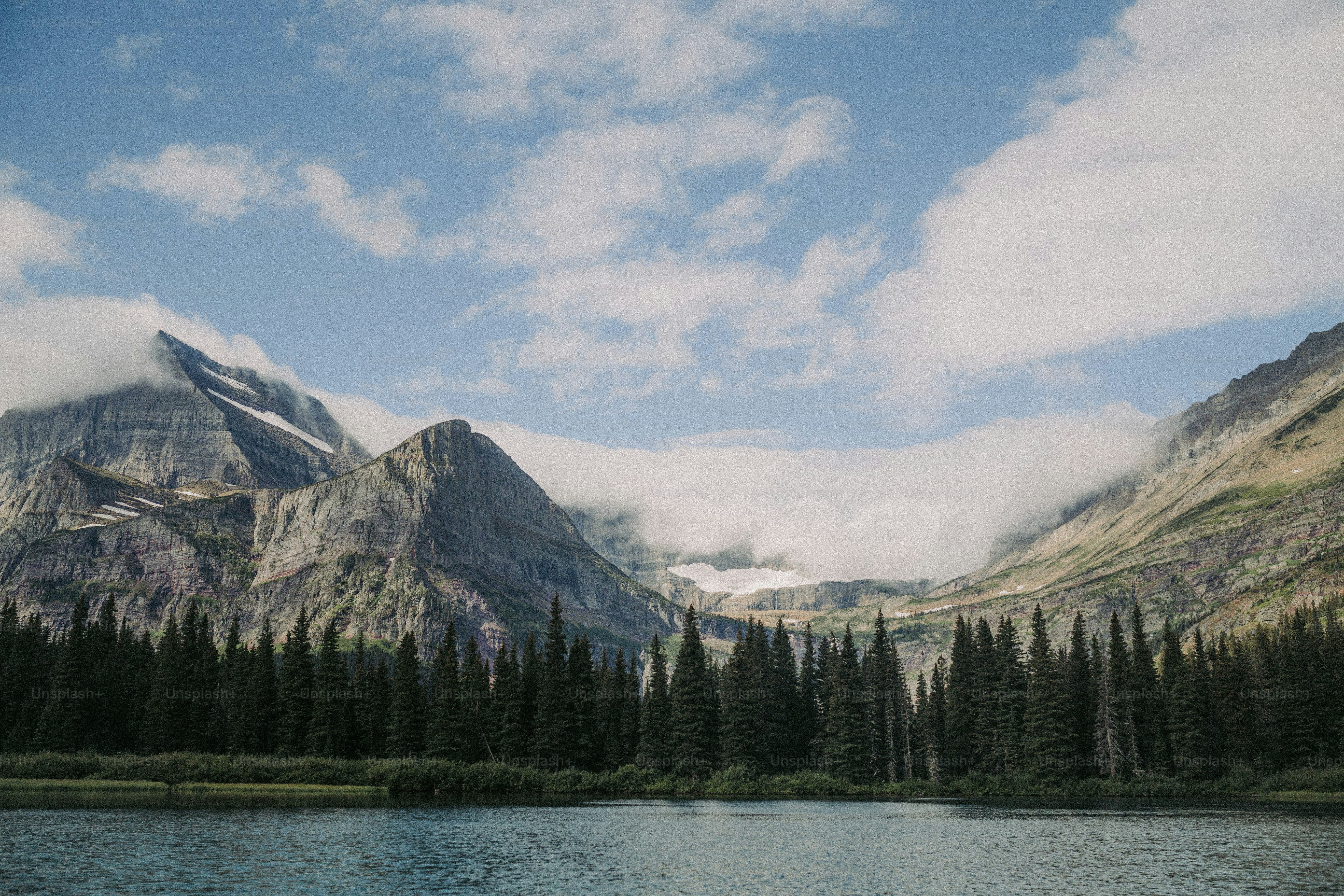 a lake surrounded by mountains and trees under a cloudy sky