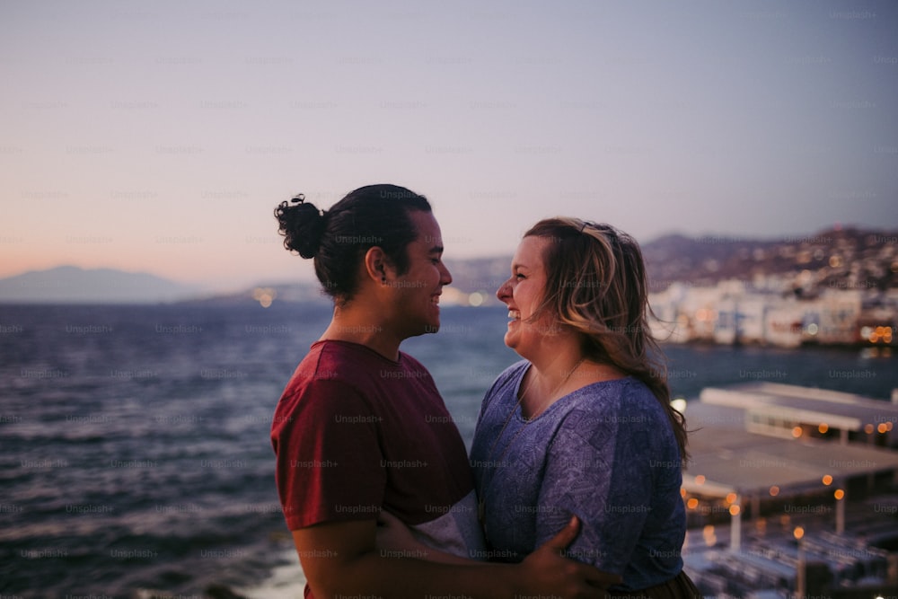 a man and a woman standing next to each other near the ocean