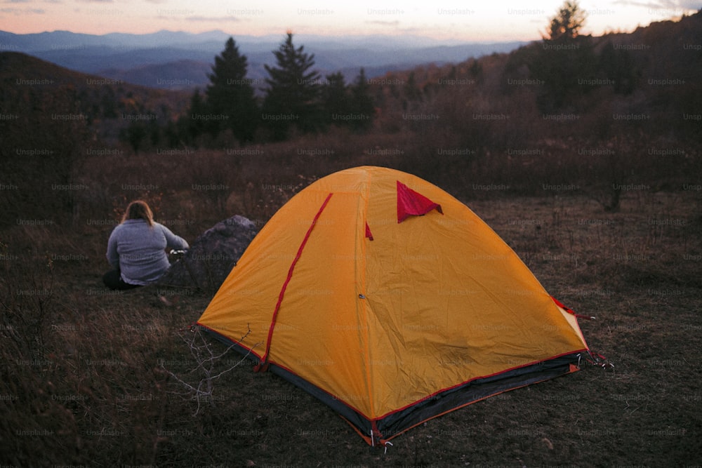 une personne assise dans un champ à côté d’une tente
