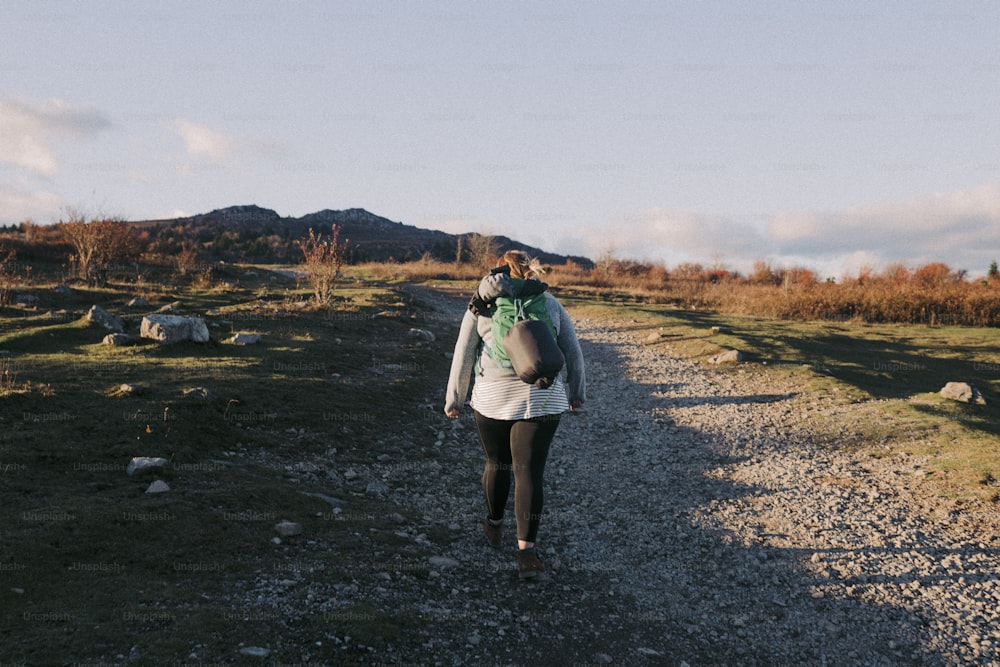 a woman walking down a dirt road with a backpack