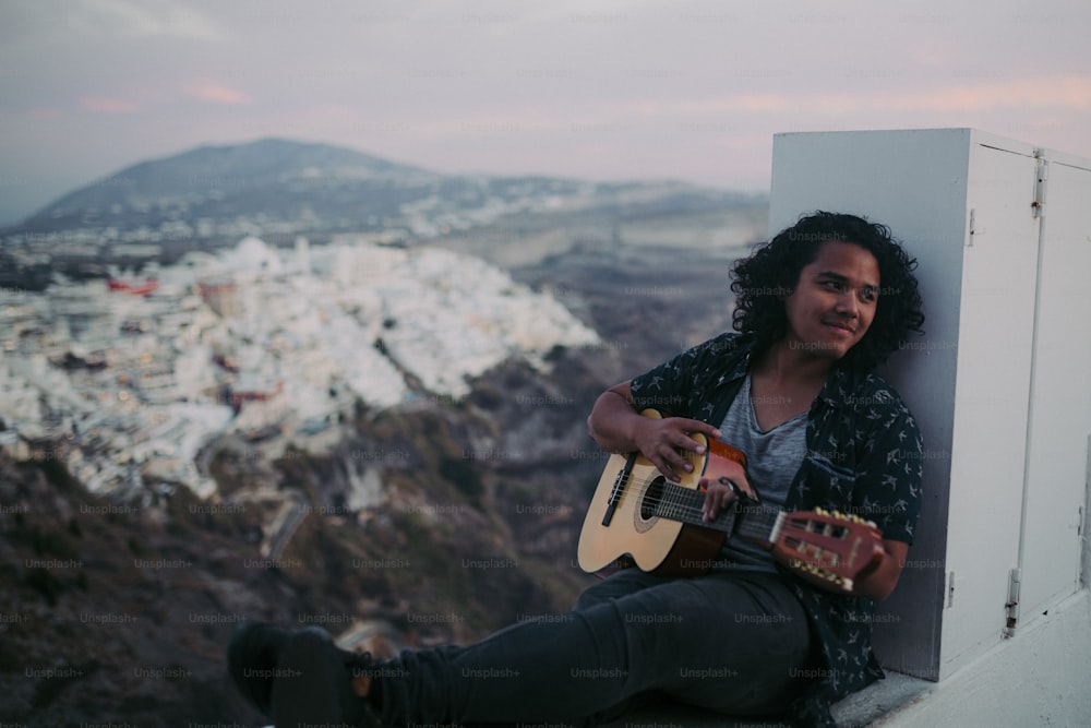 Ein Mann, der auf einem Felsvorsprung sitzt und Gitarre spielt