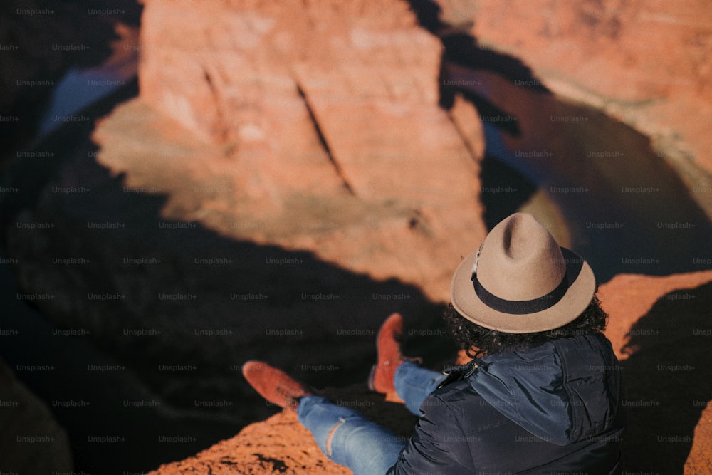 a person sitting on a rock with a hat on