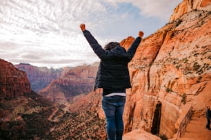 a man standing on top of a cliff with his arms in the air