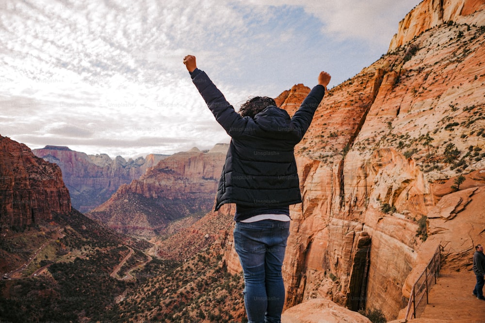 a man standing on top of a cliff with his arms in the air