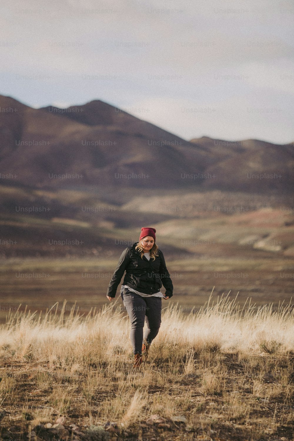 a woman walking across a dry grass covered field