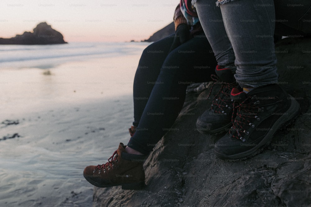 a couple of people sitting on top of a rock near the ocean