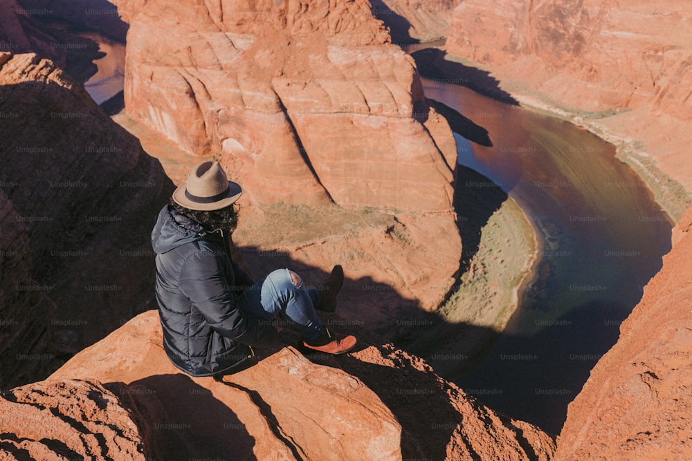 um homem sentado no topo de um penhasco ao lado de um rio