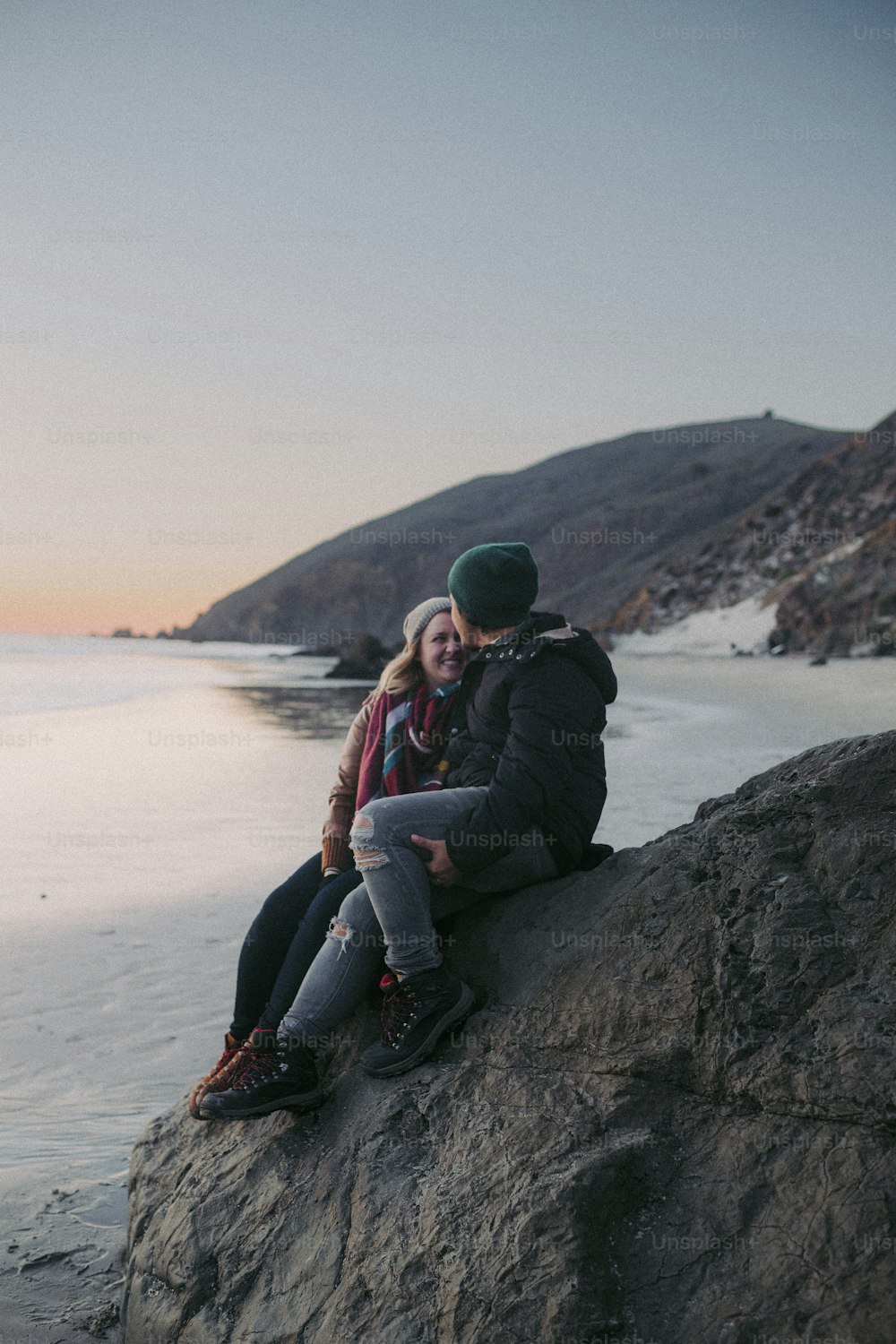 two people sitting on a rock by the water