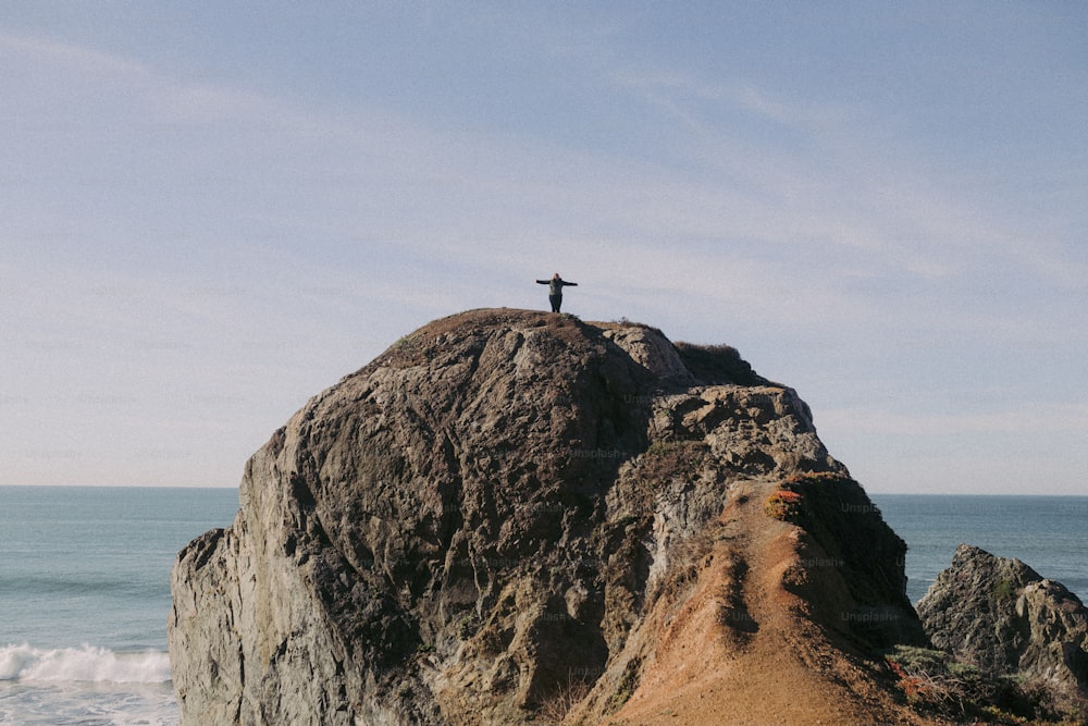 uma pessoa em pé no topo de uma rocha perto do oceano