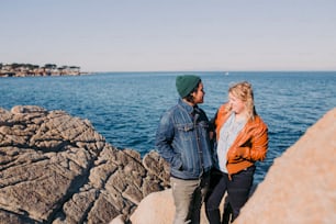 a man and a woman standing on a rock next to the ocean