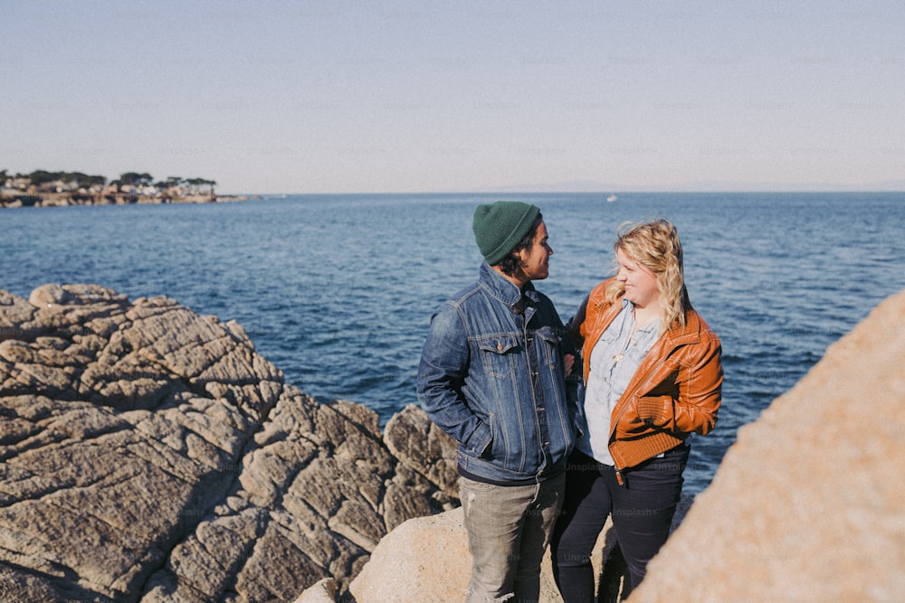um homem e uma mulher em pé em uma rocha ao lado do oceano
