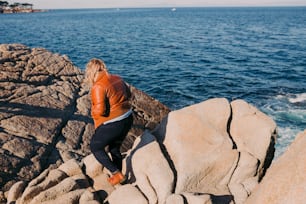 a woman sitting on a rock near the ocean