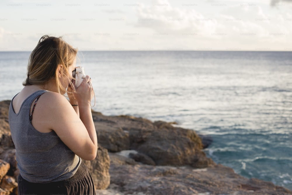 바위투성이의 해안에 서 있는 한 여자가 컵을 마시고 있다