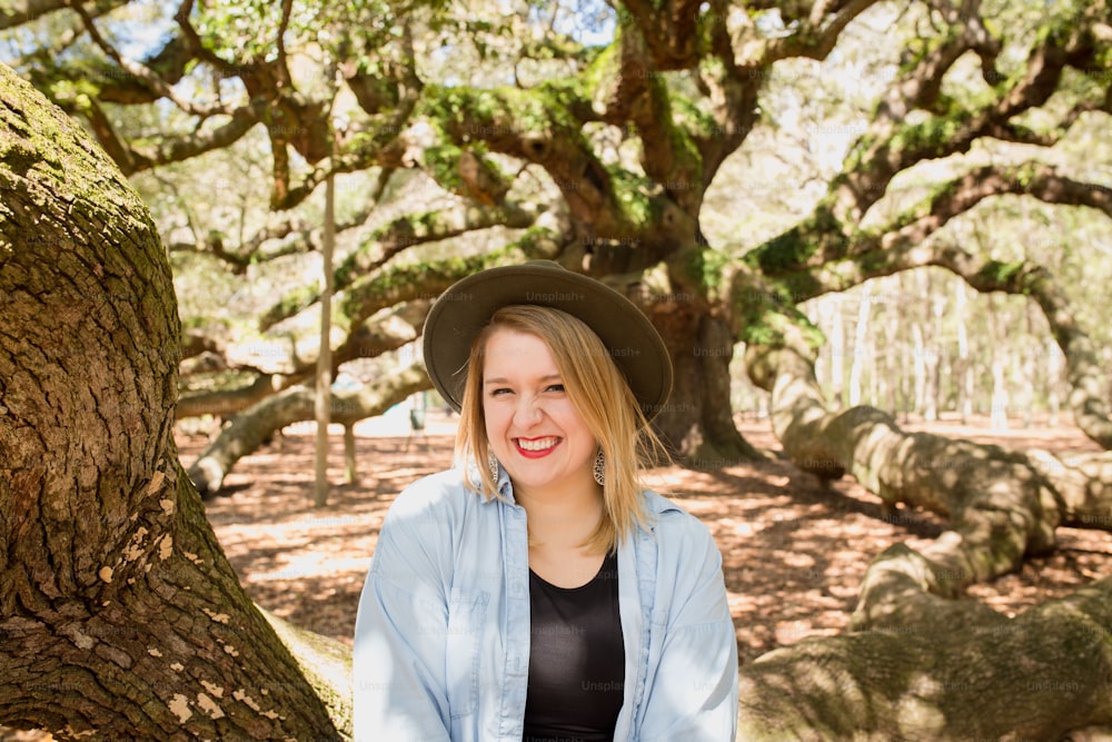 a woman wearing a hat sitting in front of a tree