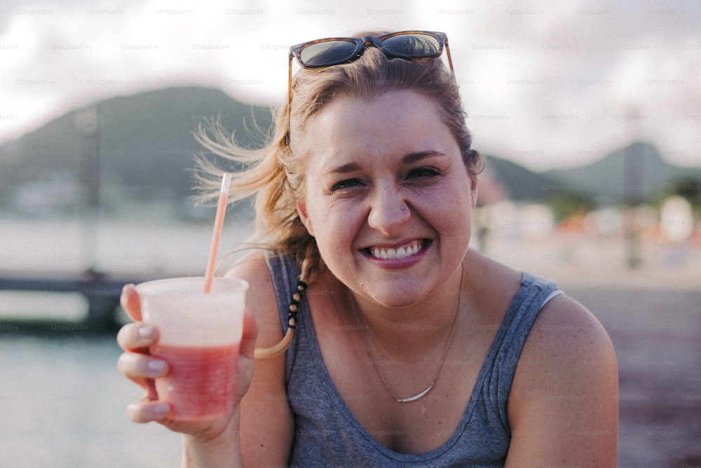uma mulher segurando uma bebida e sorrindo para a câmera