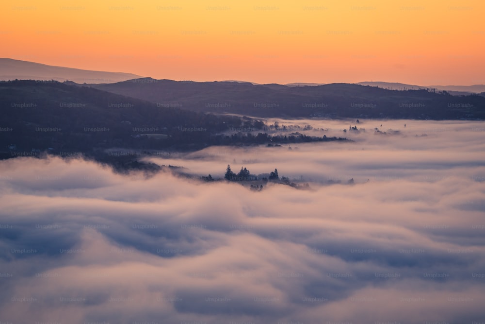 a view of a valley covered in clouds at sunset