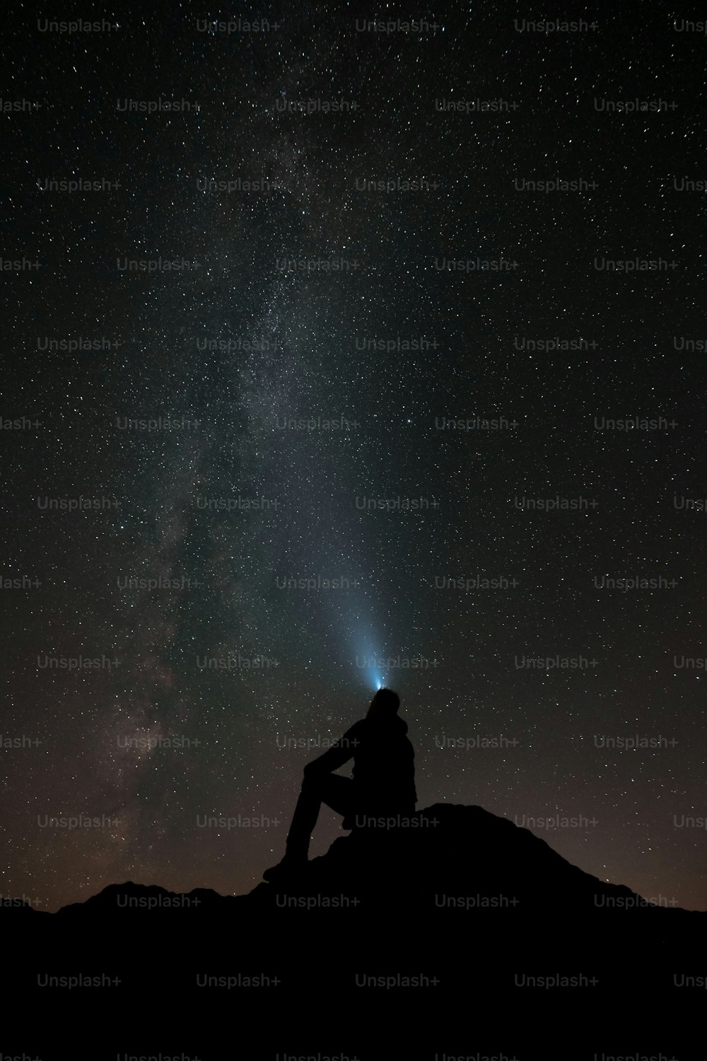 Un hombre sentado en la cima de una colina bajo un cielo nocturno lleno de estrellas