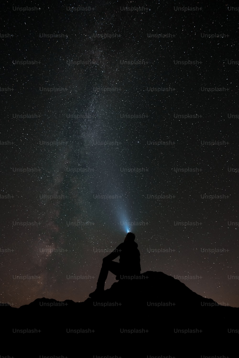 a man sitting on top of a hill under a night sky filled with stars