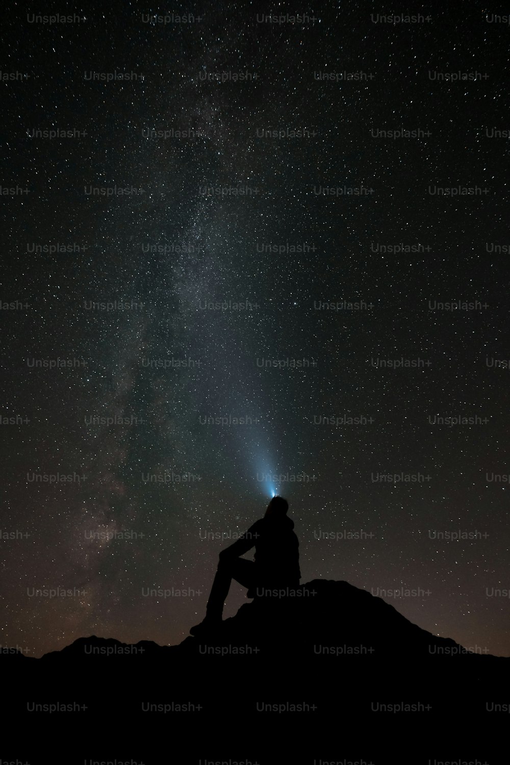 a man sitting on top of a hill under a night sky filled with stars