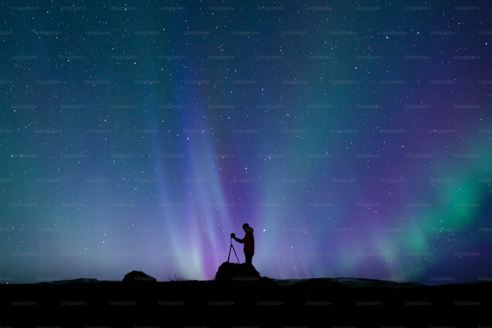 a man standing on top of a hill under a purple and green sky