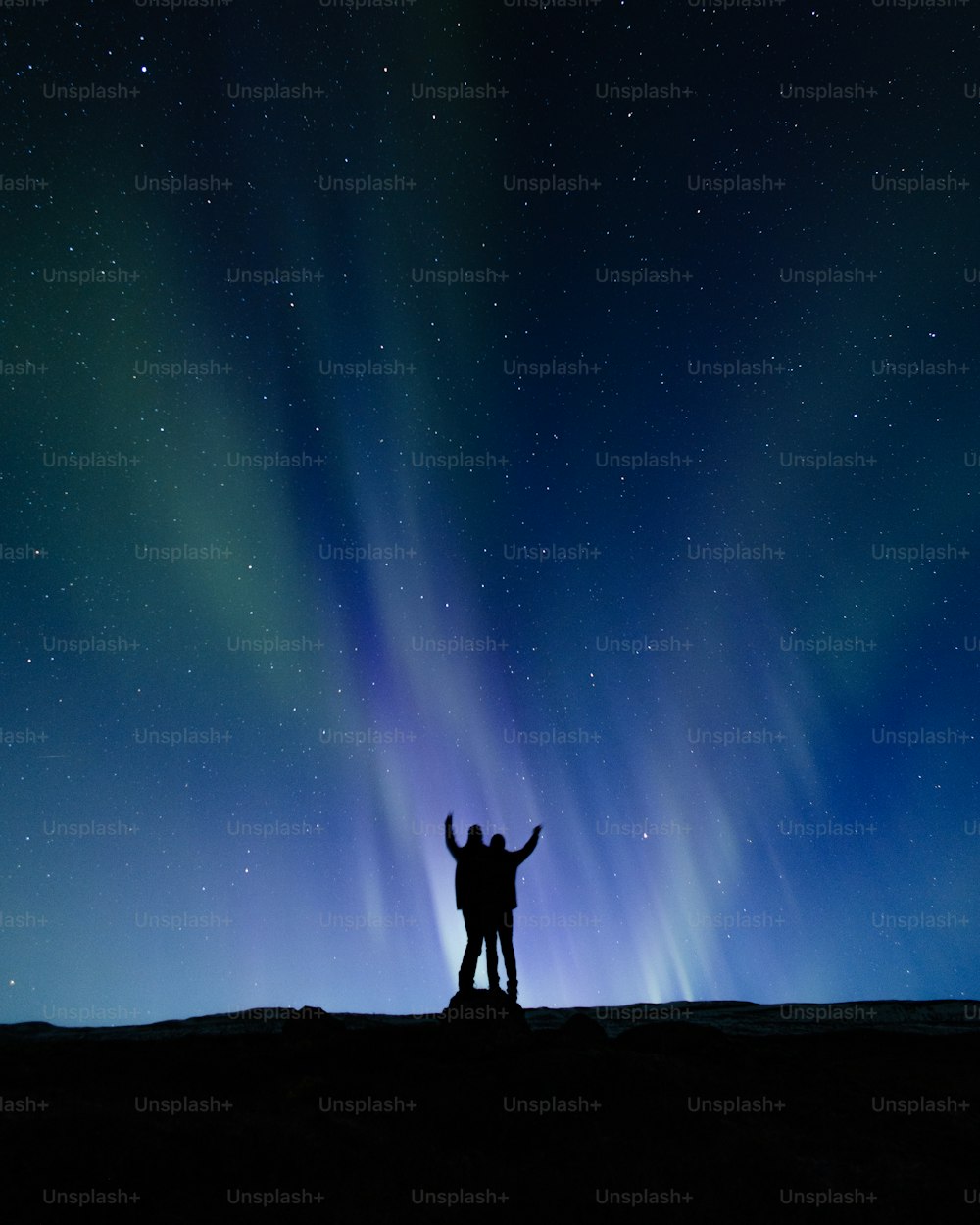 a couple of people standing on top of a hill under a sky filled with stars