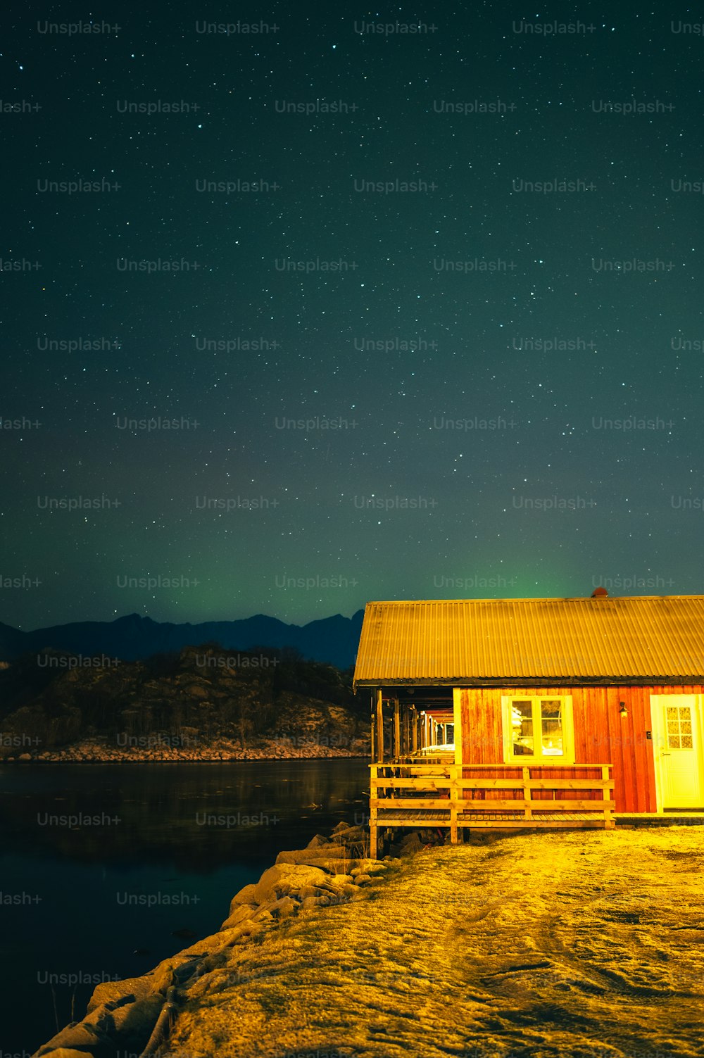 a small cabin sitting on top of a lake under a night sky