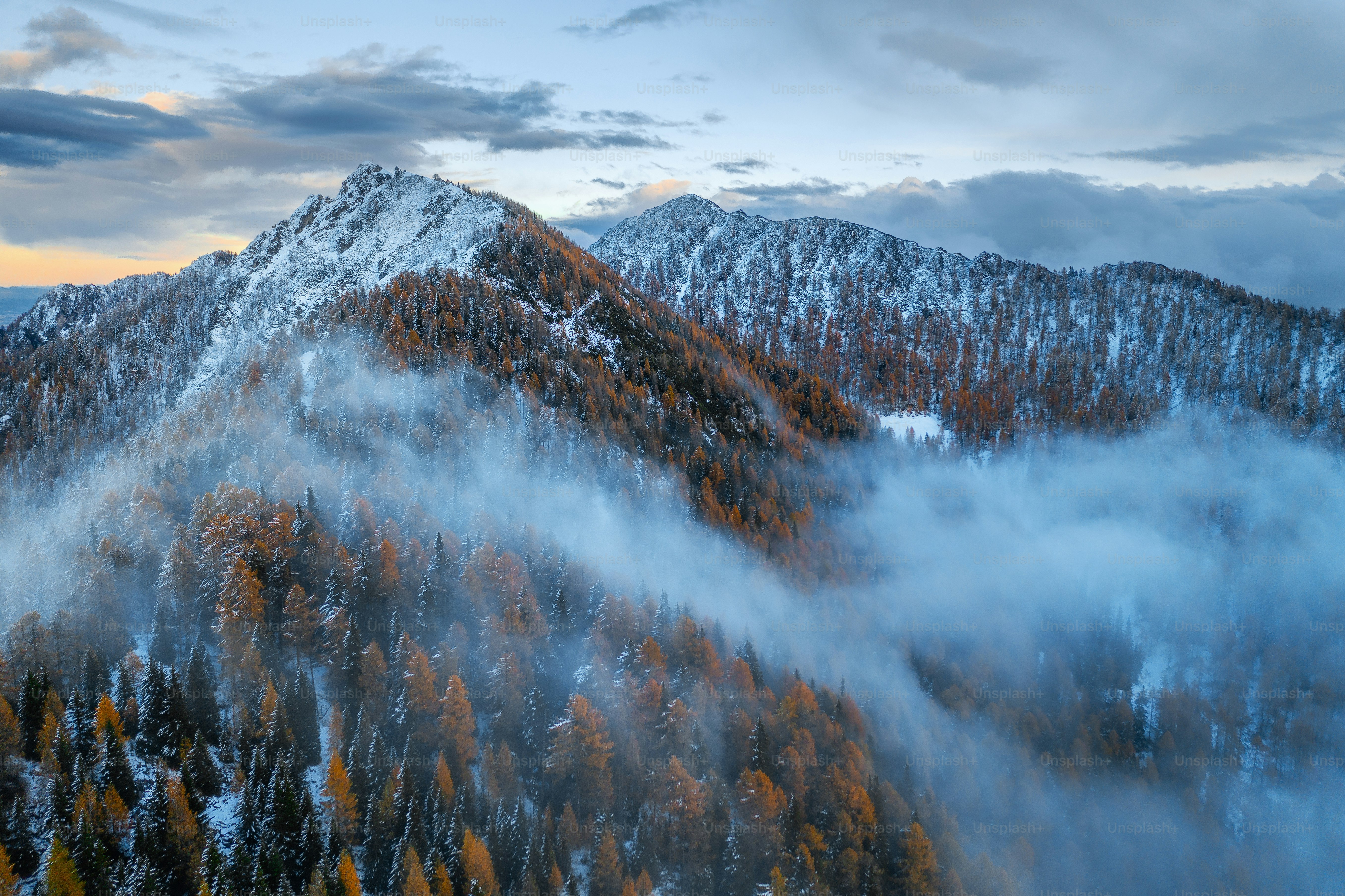 a mountain covered in clouds and trees under a cloudy sky