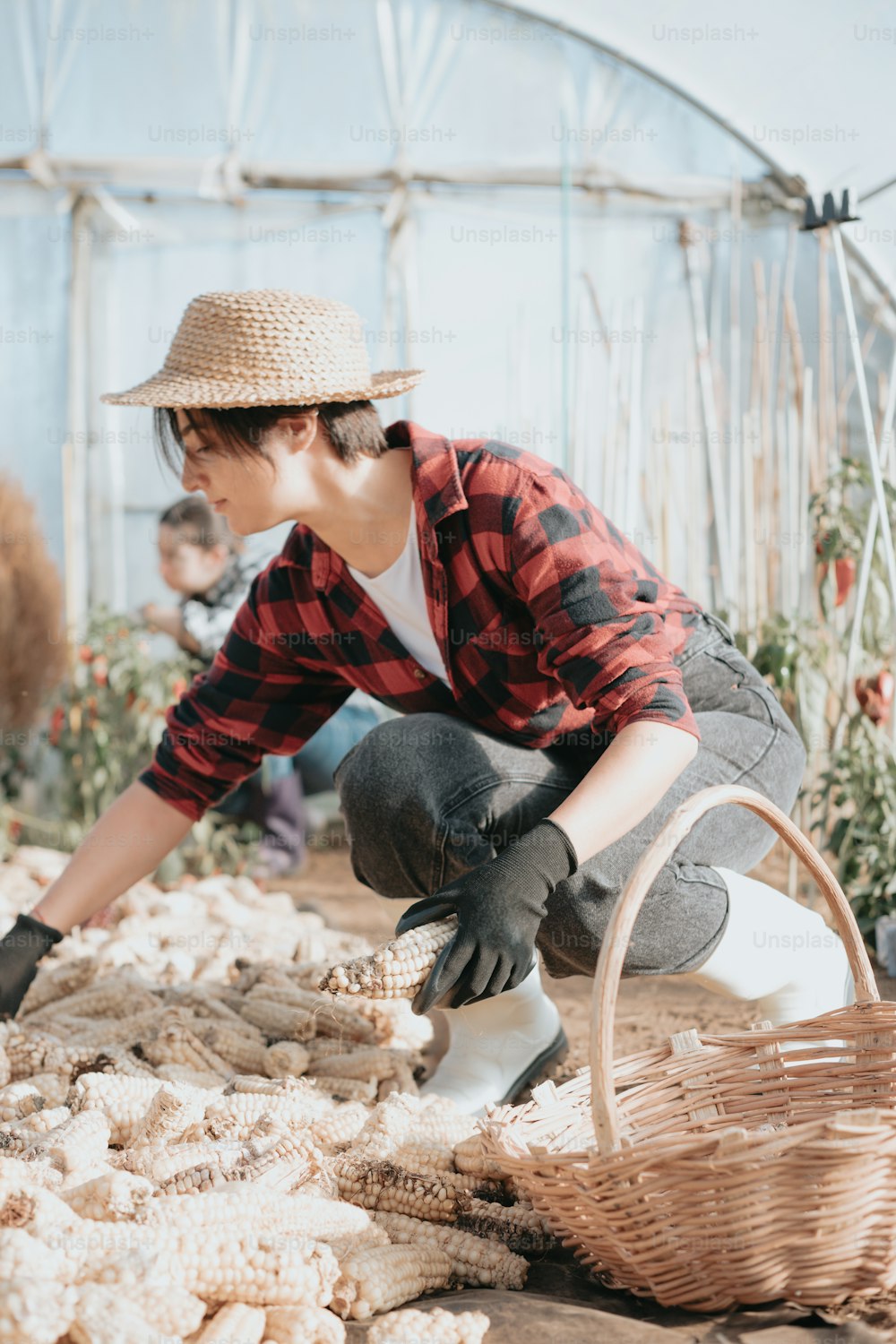 a woman in a straw hat and plaid shirt working in a garden